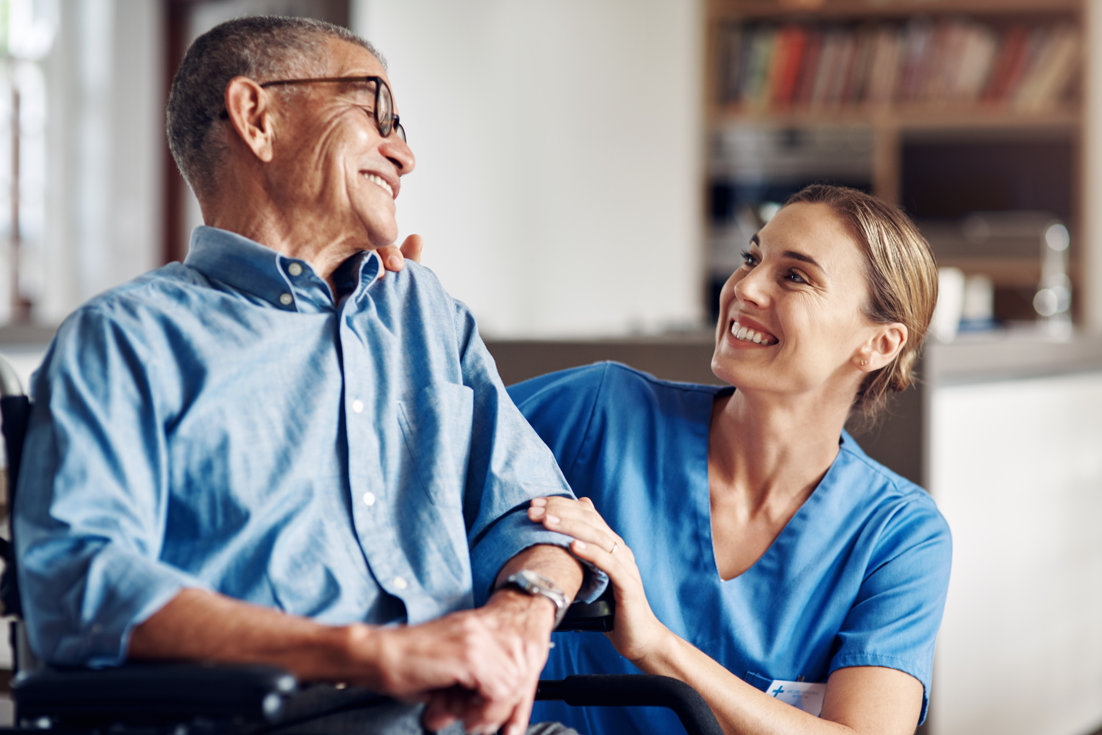 Smiling older adult in wheelchair with healthcare professional by their side.